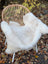 A plush off-white british isles sheepskin throw draped over a woven rattan chair for cozy style