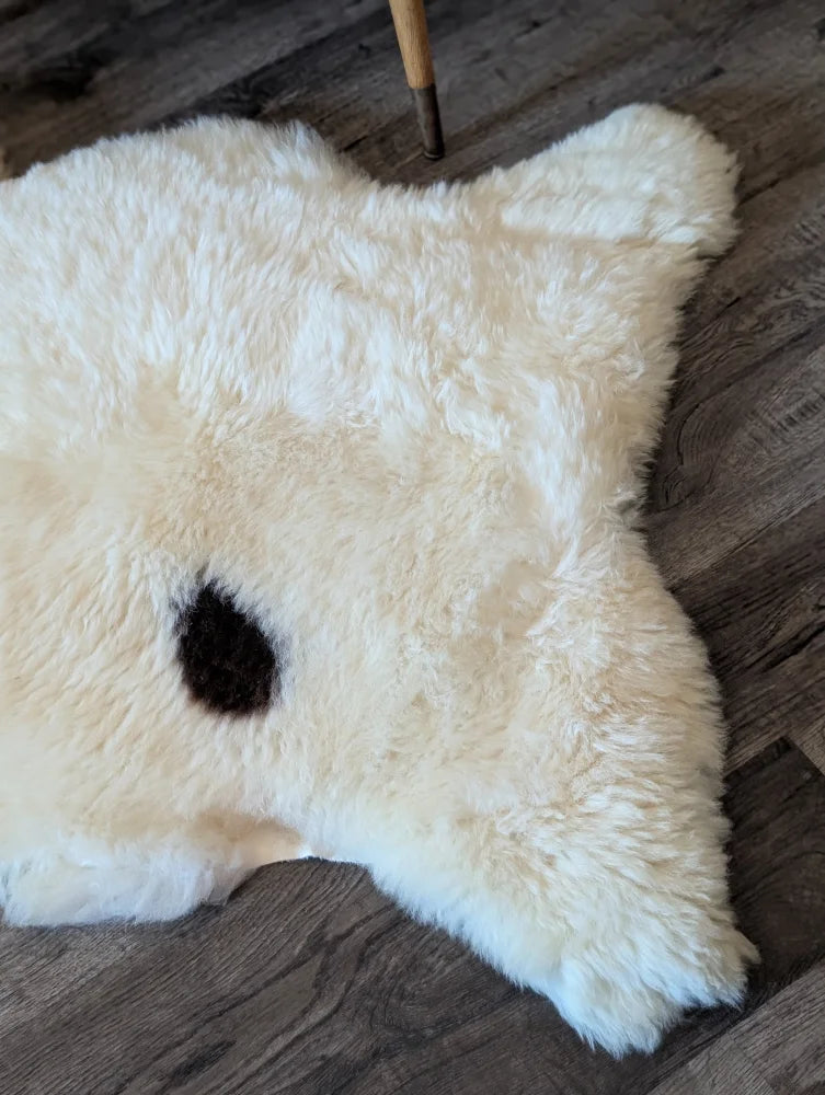 A fluffy white british isles sheepskin rug with a single black spot in the center measuring 48 by 32 inches