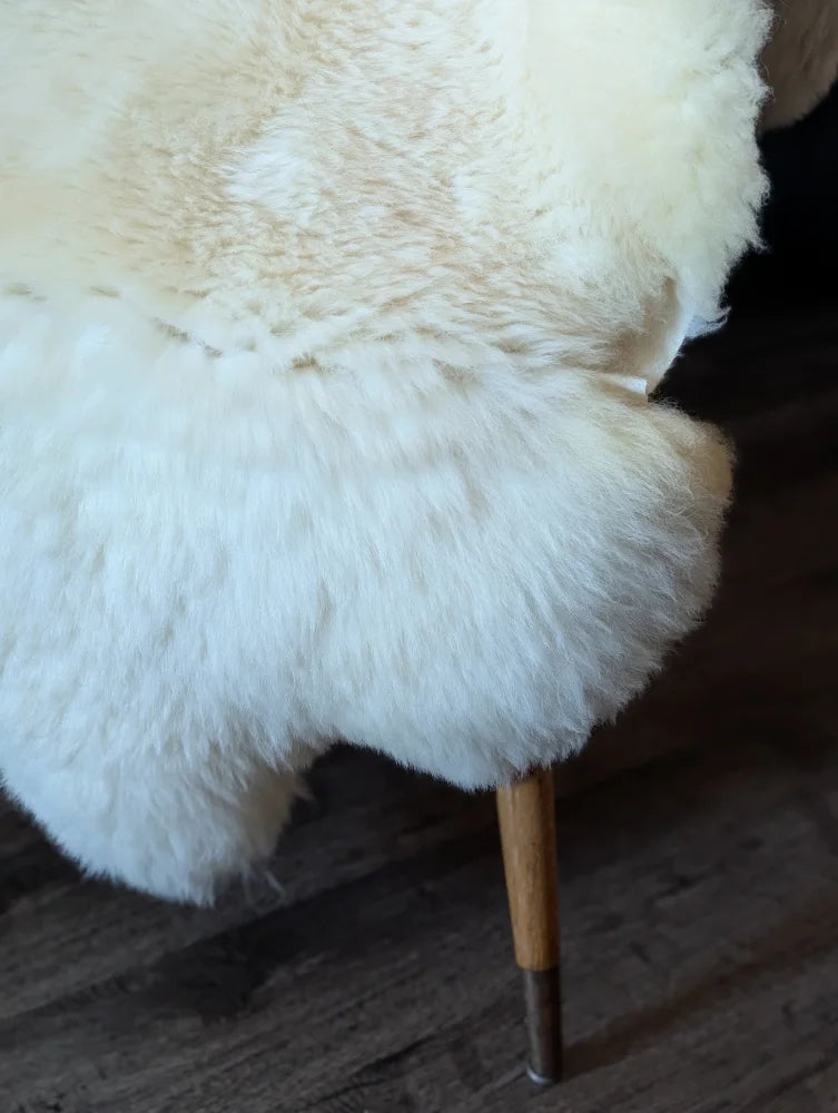 A plush off-white british isles sheepskin chair with soft fluffy texture and wooden legs perfect for cozy seating
