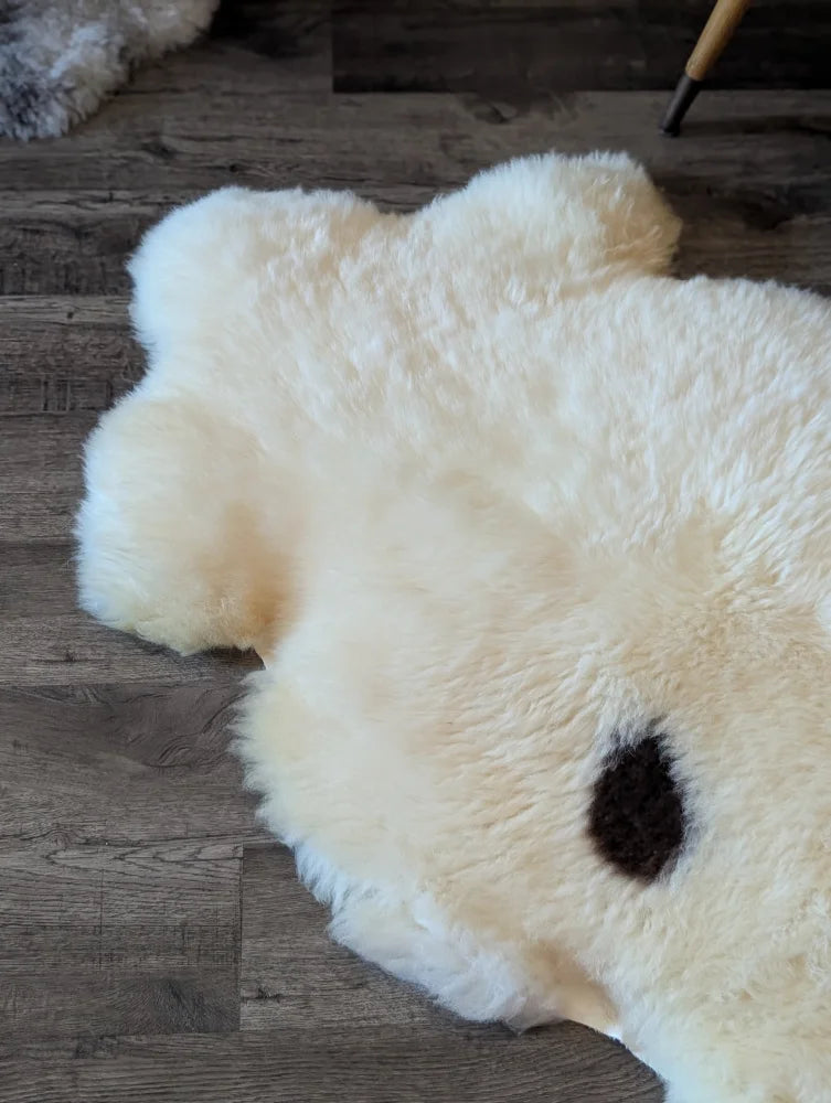 Cream-colored british isles sheepskin rug shaped like a bear with a dark brown patch on its back measuring 48 x 32 inches