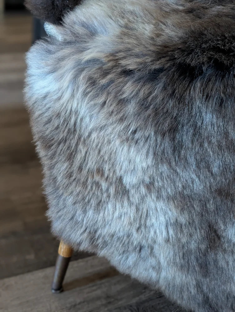 A plush gray british isles sheepskin throw draped over the back of a chair for cozy style and warmth