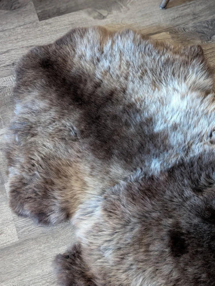 A plush british isles sheepskin rug in natural brown gray and white fur with an irregular shape measuring 47 by 31 inches