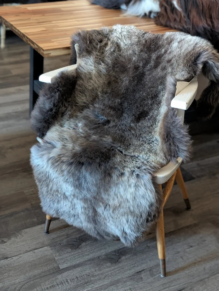 A plush natural gray and black british isles sheepskin rug draped over a wooden chair for cozy style