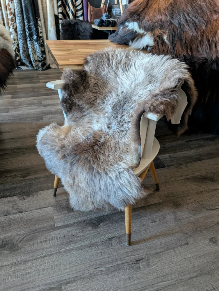 A plush natural-toned british isles sheepskin rug with fluffy texture draped over a light wooden chair back