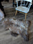 A plush british isles sheepskin rug in brown and gray natural fur lies on a wooden floor measuring 48 by 31 inches