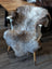 A plush british isles sheepskin rug in gray and brown draped over a wooden chair backrest for cozy decor
