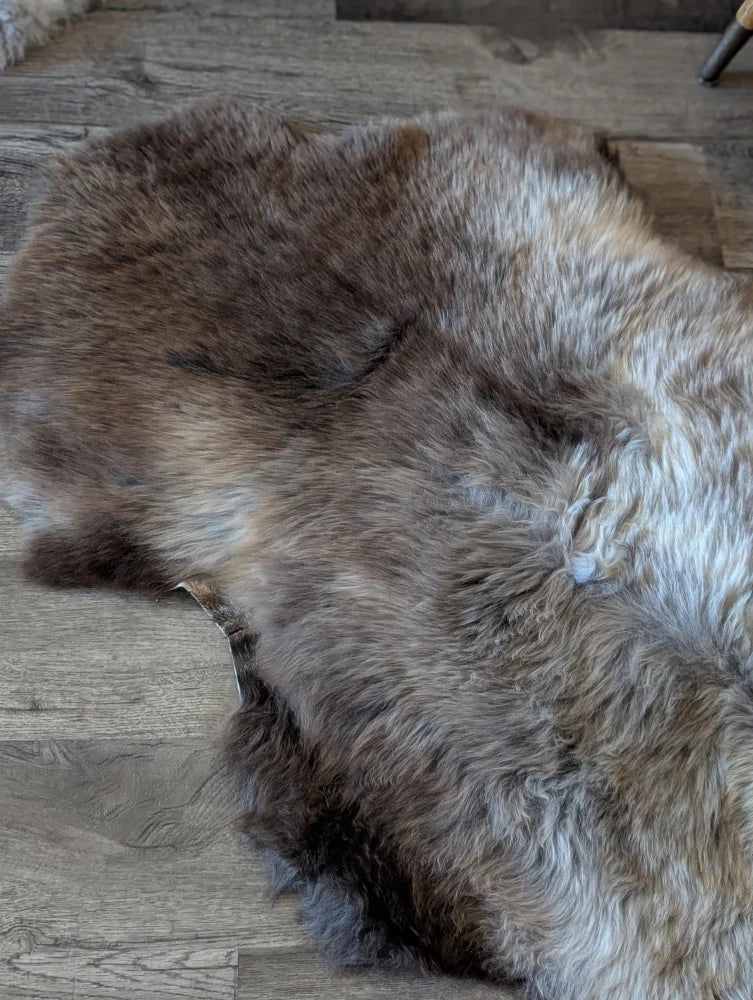 A plush british isles sheepskin rug in natural brown and gray with thick soft fur spread on a wooden floor