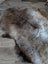 A plush british isles sheepskin rug in natural brown and gray with thick soft fur spread on a wooden floor