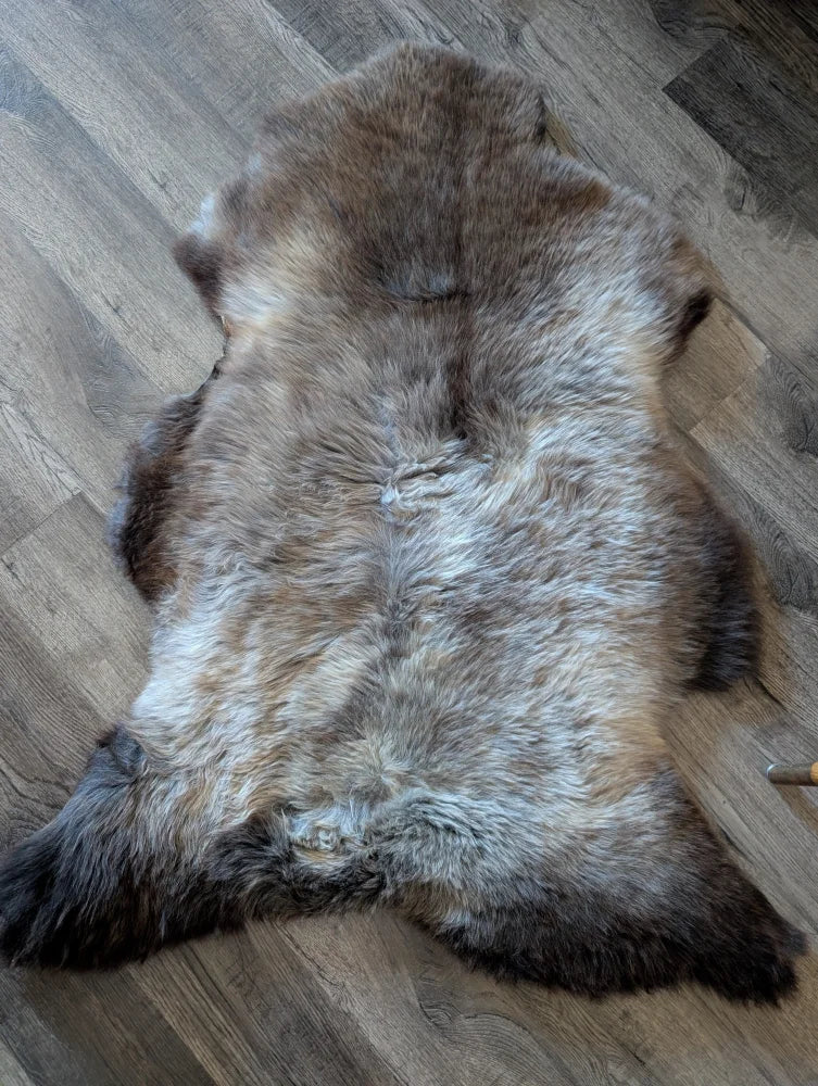 A natural brown and gray british isles sheepskin rug with soft dense fur lies flat on a wooden floor