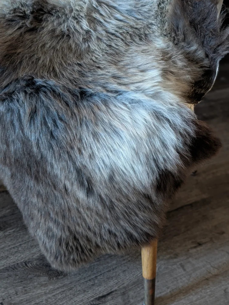 A plush gray and black british isles sheepskin throw draped over the back of a chair perfect for cozy use