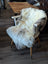 A plush cream and gray british isles sheepskin rug draped over a white wooden chair with tapered legs