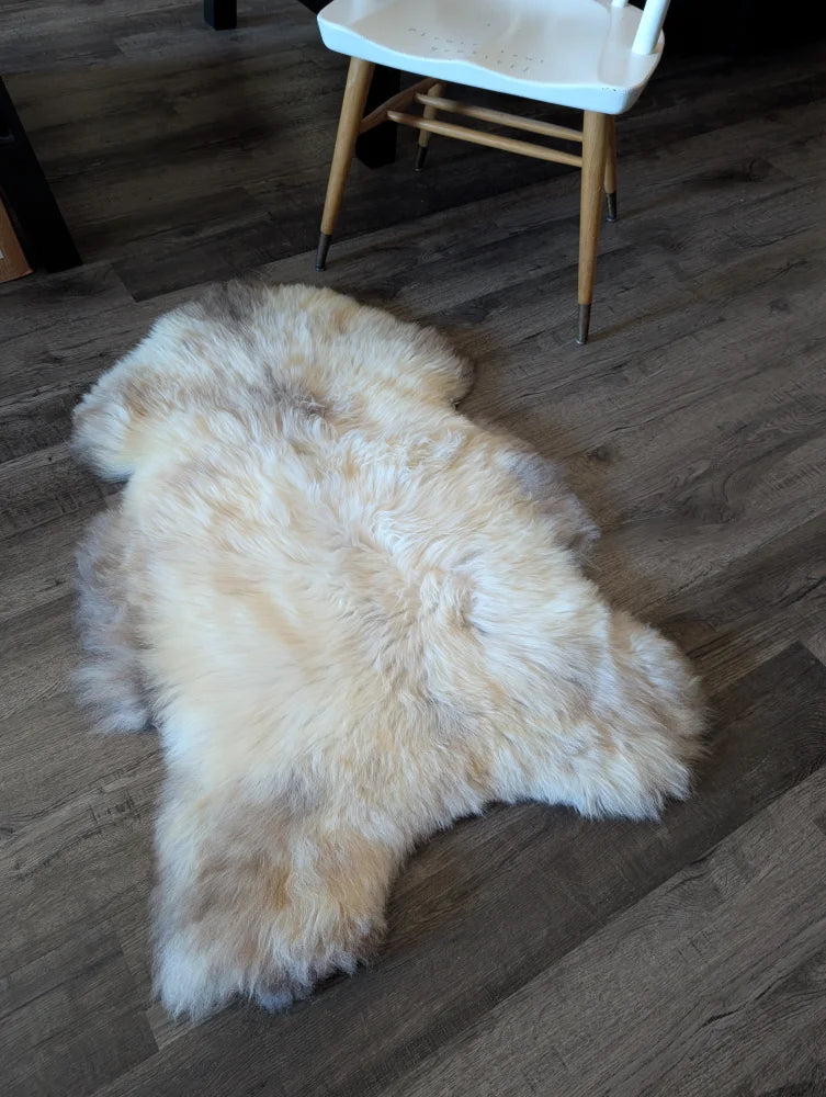 A plush cream-colored british isles sheepskin rug with soft fluffy texture on wooden floor perfect for cozy spaces