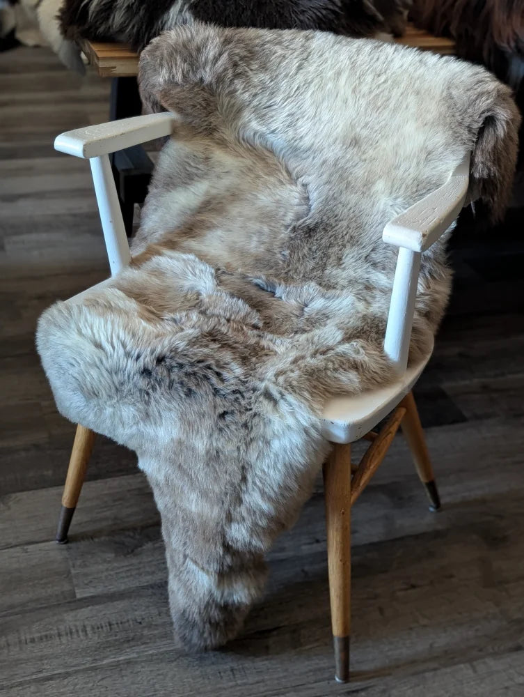 A plush british isles sheepskin rug in natural grayish brown draped over a white wooden chair seat