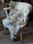 A plush british isles sheepskin rug in natural grayish brown draped over a white wooden chair seat