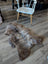 A plush natural brown and gray british isles sheepskin rug with soft thick fur lies flat on a wooden floor