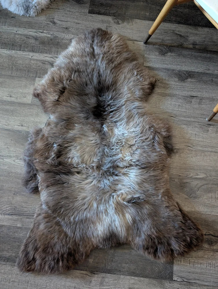 A plush british isles sheepskin rug in brown and gray tones lies flat on a wooden floor for cozy decor