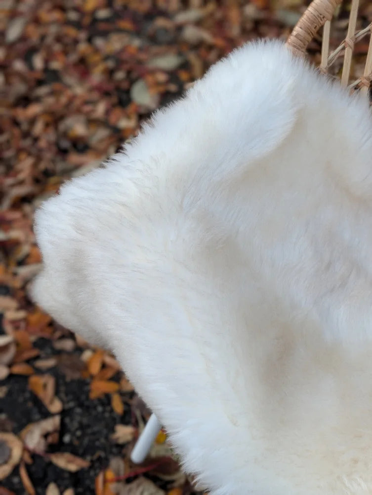 A plush white faux fur throw draped over a wicker chair made from very soft british isles sheepskin