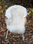 A plush off-white british isles sheepskin blanket draped over a wicker chair with white metal legs