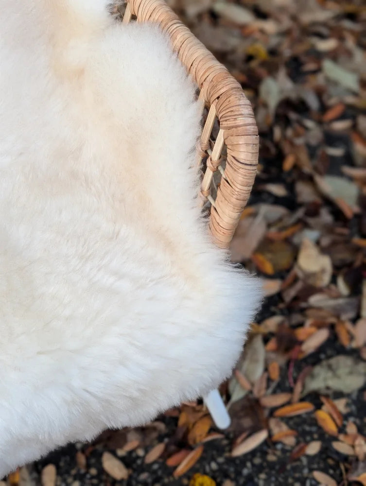 A plush off-white very soft british isles sheepskin throw draped over the woven wicker edge of a chair