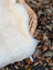 A plush off-white very soft british isles sheepskin throw draped over the woven wicker edge of a chair
