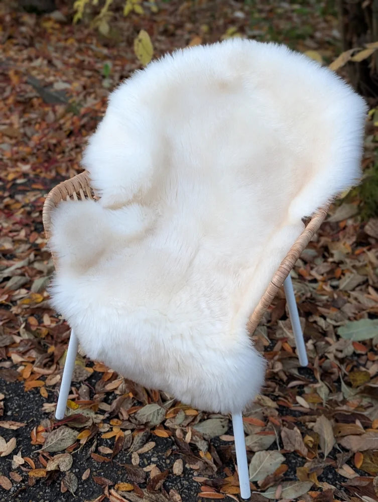 A very soft off-white british isles sheepskin rug draped over a woven wicker chair with white metal legs