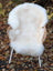 A plush off-white british isles sheepskin rug draped over a wicker chair with white legs for soft comfort