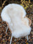 White fluffy british isles sheepskin chair cover draped over wicker chair with white legs very soft texture