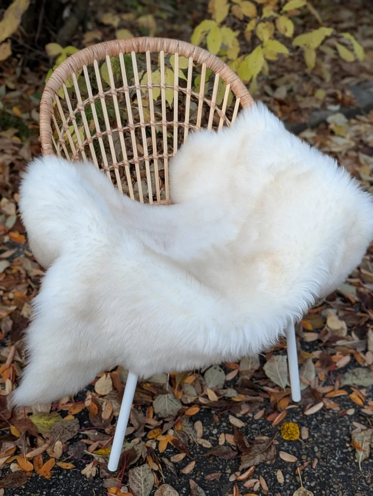 White faux fur throw blanket made from soft british isles sheepskin draped over a wicker chair