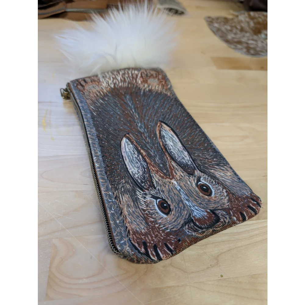 A hand-painted leather coin purse with two brown and gray rabbits and a fluffy white sheepskin tail pom pom