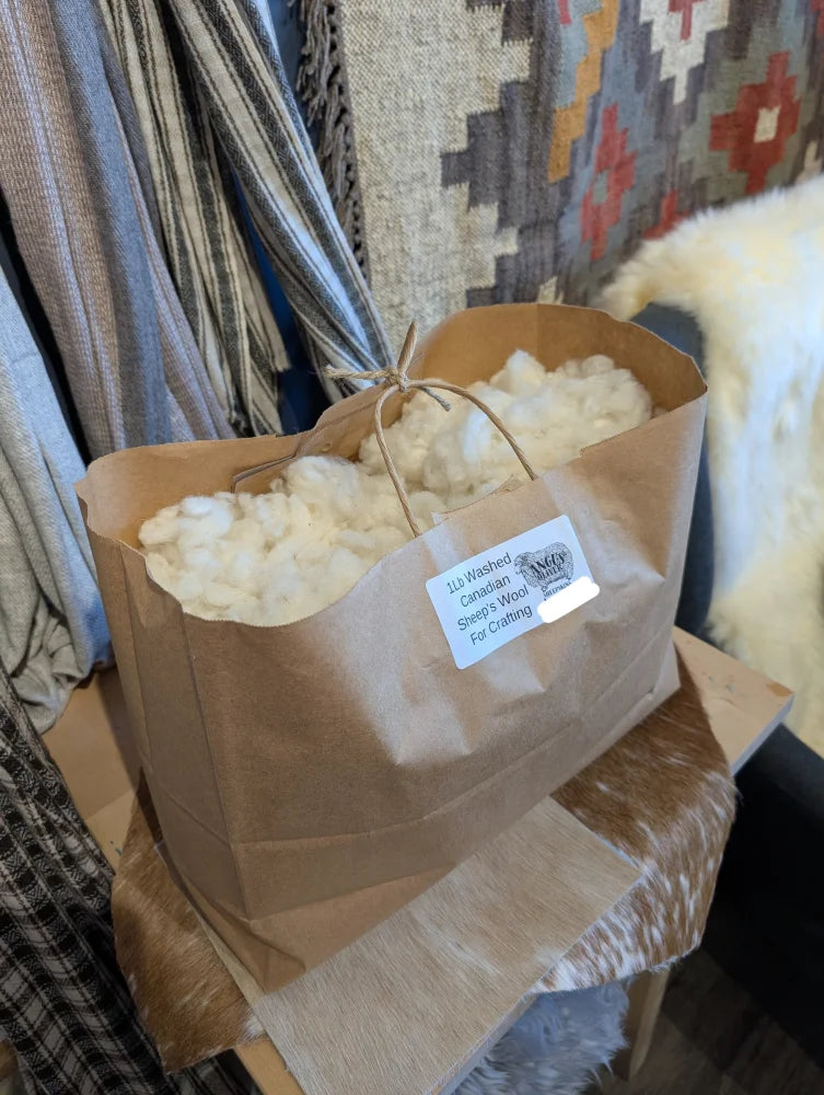 A brown paper bag of fluffy white canadian washed wool tied with twine labeled for crafting projects