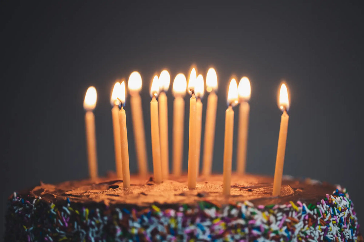A chocolate cake adorned with colorful rainbow sprinkles and ten lit yellow candles.