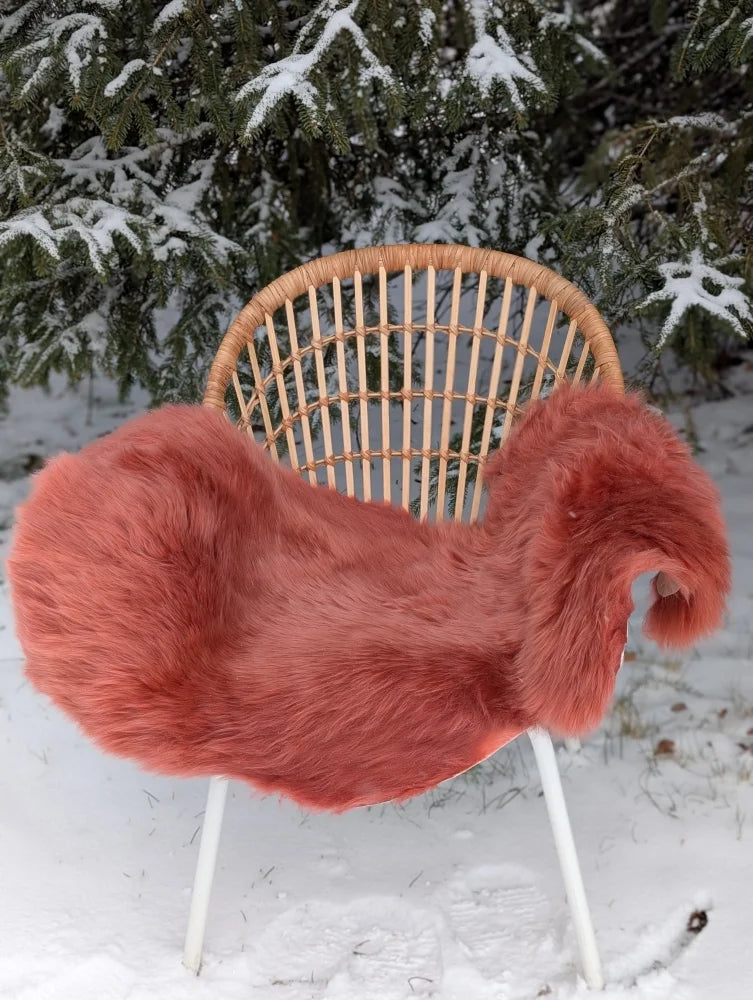 A plush coral pink merino sheepskin chair cover with soft fluffy texture and slightly irregular edges in dusty pink