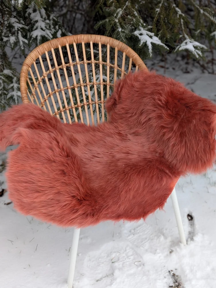A coral merino sheepskin plush faux fur throw in dusty pink draped over a wicker chair meeting reach standards