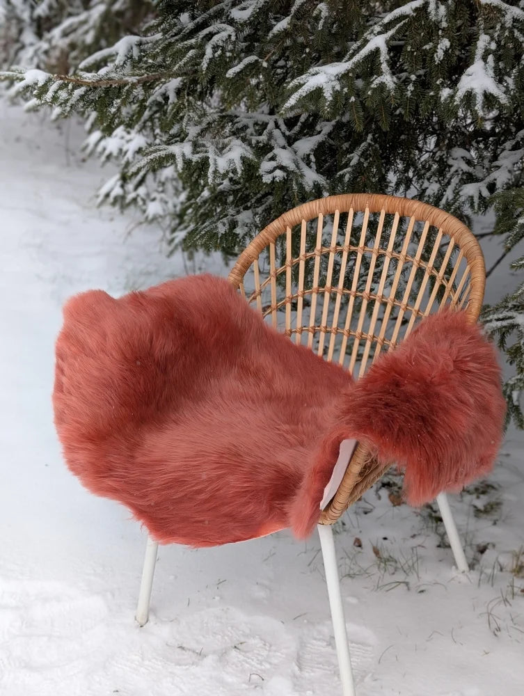 A coral pink merino sheepskin faux fur throw draped over a wicker chair with white metal legs in dusty pink