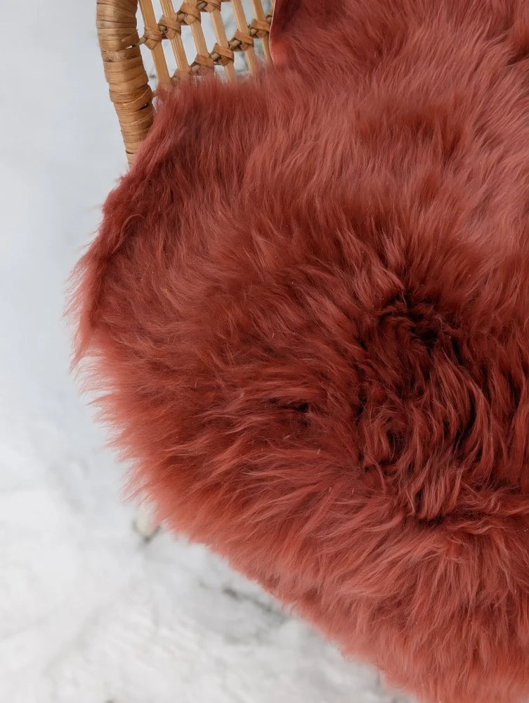 A plush coral merino sheepskin throw in dusty pink tones with soft long fibers draped over a wicker chair
