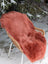 A coral merino sheepskin throw in dusty pink draped over a wicker chair perfect for cozying up at home