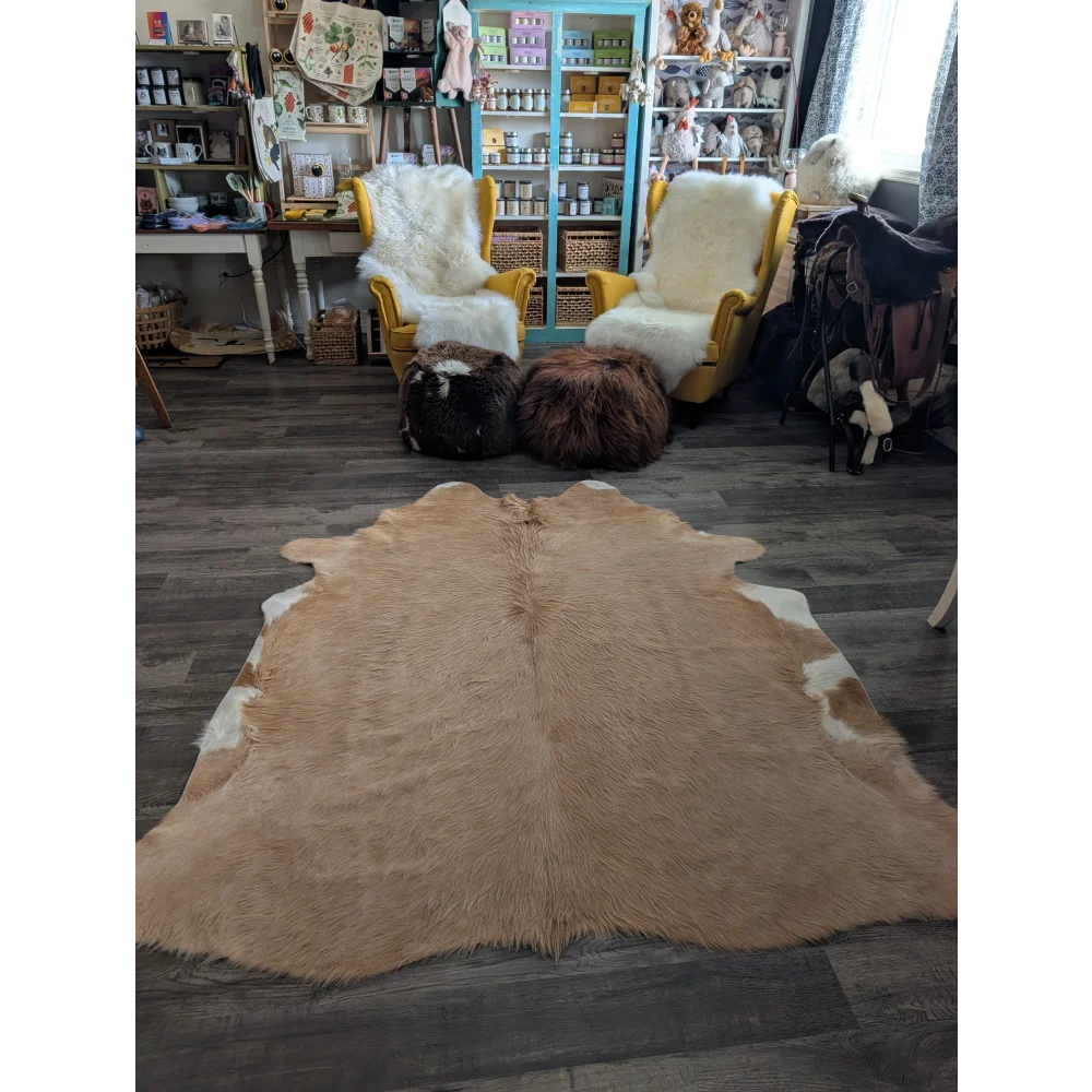 A large cowhide rug with beautiful tan and white colors and unique characteristics lies flat showcasing its soft texture
