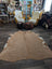 A large cowhide rug with beautiful tan and white colors and unique characteristics lies flat showcasing its soft texture