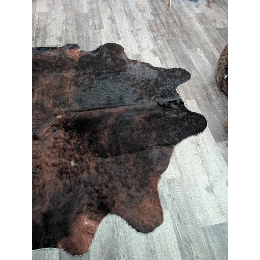 A large cowhide rug with rich dark brown and black textured fur showing unique characteristics and beauty