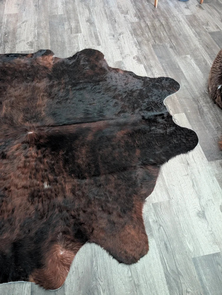 A large cowhide rug with rich dark brown and black textured fur showing unique characteristics and beauty