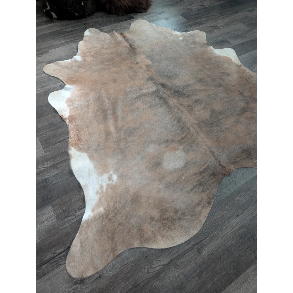 A large cowhide rug in natural tones with a soft textured surface and unique irregular edges perfect for beautiful rugs