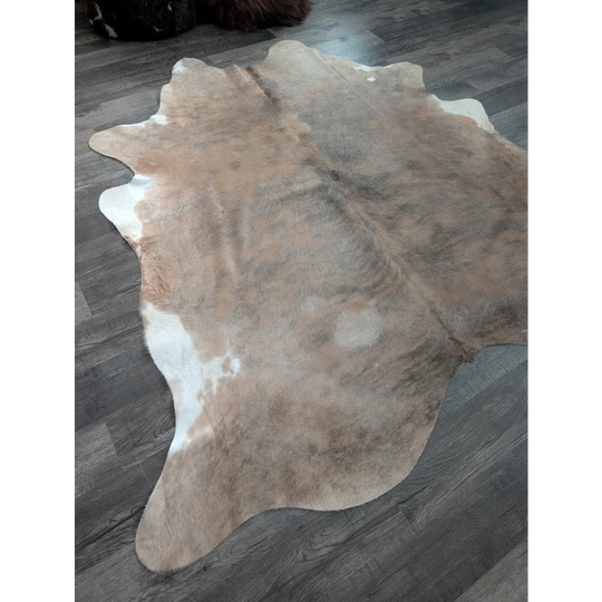 A large cowhide rug in natural tones with a soft textured surface and unique irregular edges perfect for beautiful rugs