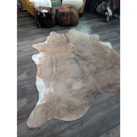 A large cowhide rug with a natural tan and white pattern and soft textured surface showcasing unique characteristics