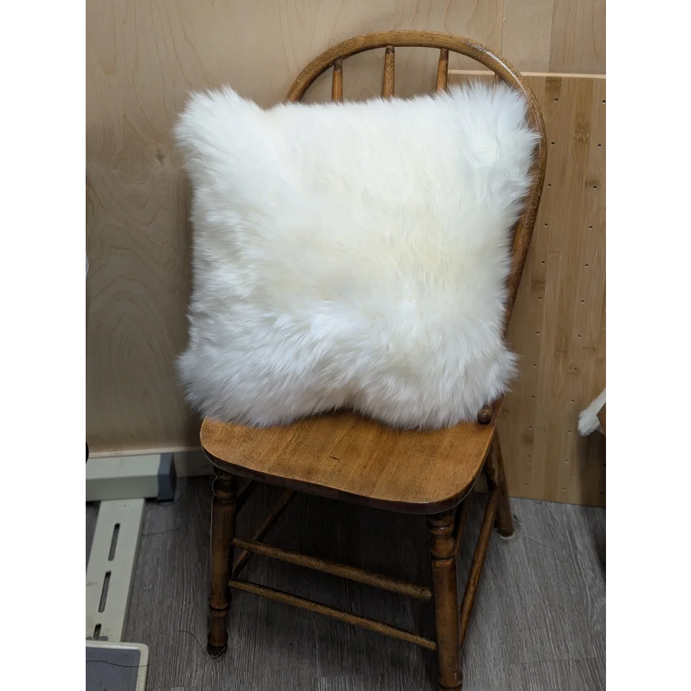 White fluffy merino sheepskin cushion resting on wooden chair by angus oliver canada