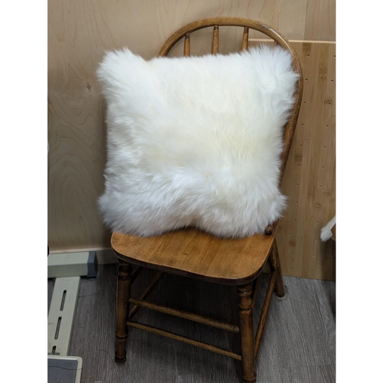White fluffy merino sheepskin cushion resting on wooden chair by angus oliver canada