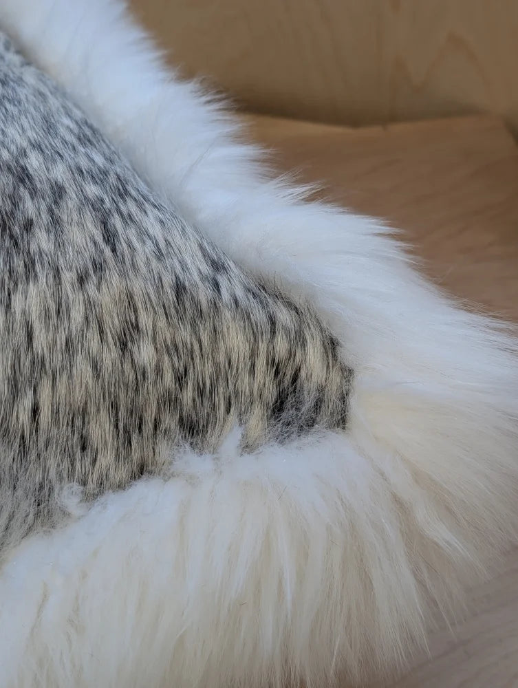 A cowhide and merino sheepskin cushion with a mottled gray and white plush throw and soft white border by Angus Oliver Canada
