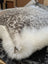 A plush cowhide and merino sheepskin cushion with speckled gray top and fluffy white trim by angus oliver canada