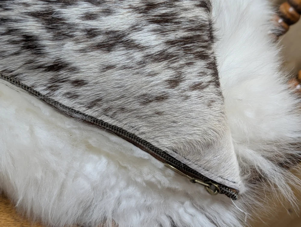 A cozy cowhide and merino sheepskin cushion with gray black speckled exterior and plush white lining by angus oliver canada