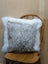 A cozy cowhide and merino sheepskin cushion with speckled gray center and fluffy white fur trim by angus oliver canada