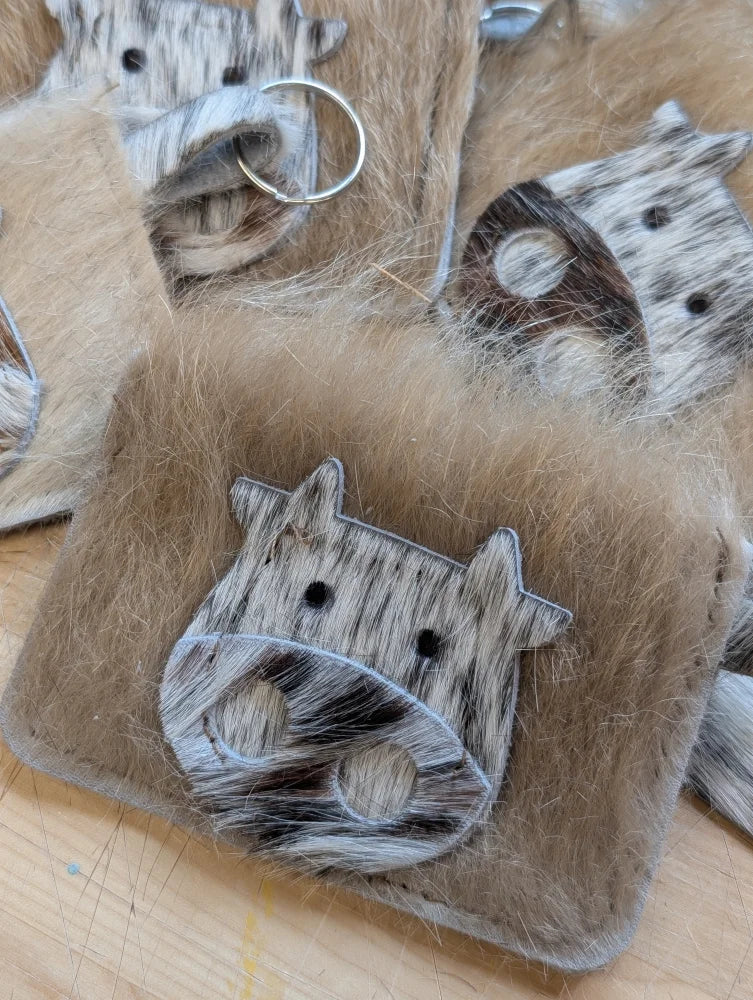 A plush fuzzy brown cow keychain card holder with a black and white spotted face and stitched details